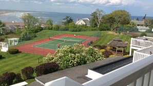 A tennis court with a view of the ocean and houses in the background.