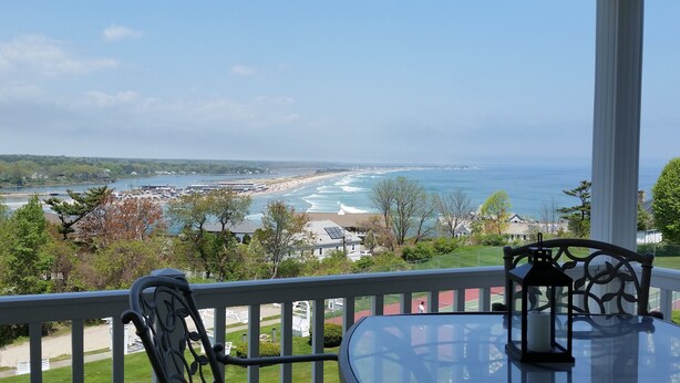 A balcony with a view of the ocean and beach, a table with a glass top, and a metal railing.