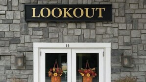 A building entrance with a sign reading 'LOOKOUT' above double doors, number 55, and baskets with flowers on the glass doors.