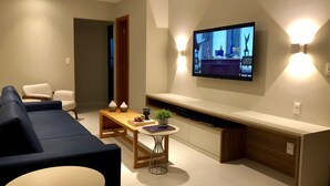 A modern living room with a sofa, a coffee table, and a TV mounted on the wall. - Beachfront village with natural pools near the condominium! (Camaçari)
