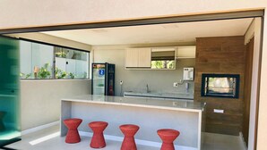 A modern kitchen with a glass partition, a built-in oven, and a small island with stools. - Beachfront village with natural pools near the condominium! (Camaçari)