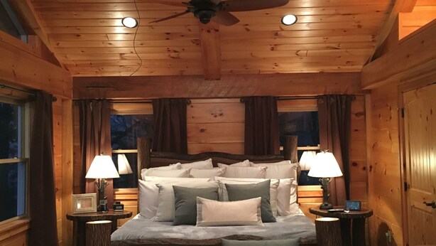 A cozy log cabin bedroom with a bed, bedside tables, a bench, and a ceiling fan.