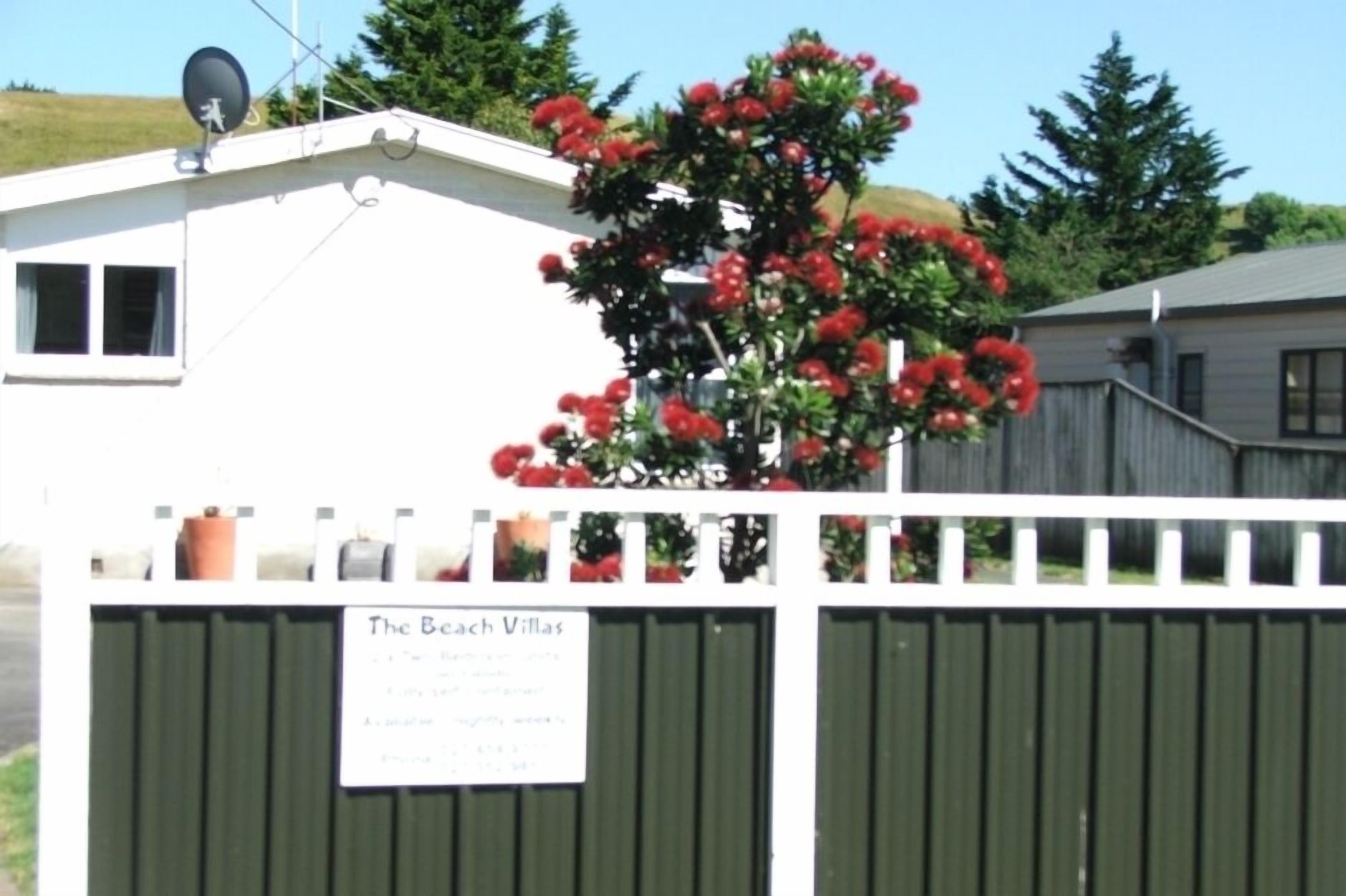 Une propriété clôturée, avec une pancarte indiquant « The Beach Villas » et une antenne parabolique sur le toit.