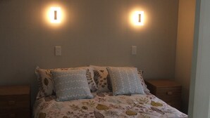Una cama con ropa de cama floral, dos luces empotradas en la pared y una mesita de noche a cada lado.
