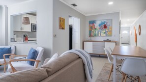 Un salon moderne avec un canapé, des fauteuils, une table à manger et une cuisine en arrière-plan.