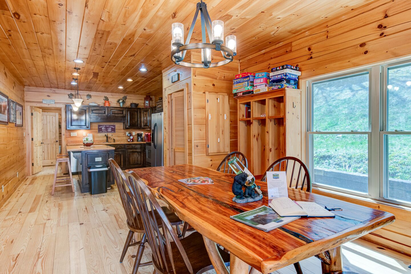 A wooden cabin interior with a dining table, chairs, a chandelier, and a view of the outdoors.
