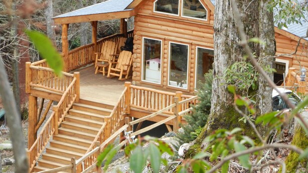 A wooden cabin with a deck, outdoor seating, and a staircase leading to the entrance. - CREEKSIDE LOG HOME: NEXT TO CREEK / CLOSE TO TOWN / HOT TUB / TRAILS / PETS OK (Black Mountain)