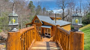 A wooden bridge leading to a log cabin with a porch and a chimney. - CREEKSIDE LOG HOME: NEXT TO CREEK / CLOSE TO TOWN / HOT TUB / TRAILS / PETS OK (Black Mountain)