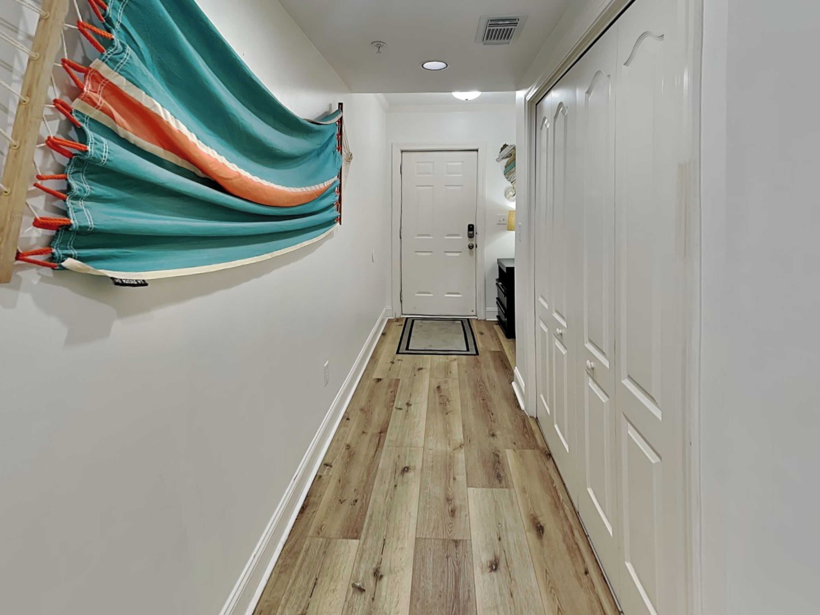 A hallway with wooden flooring, white walls, and a door at the end.