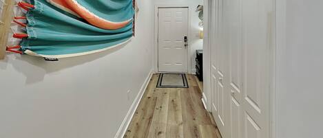 A hallway with wooden flooring, white walls, and a door at the end.
