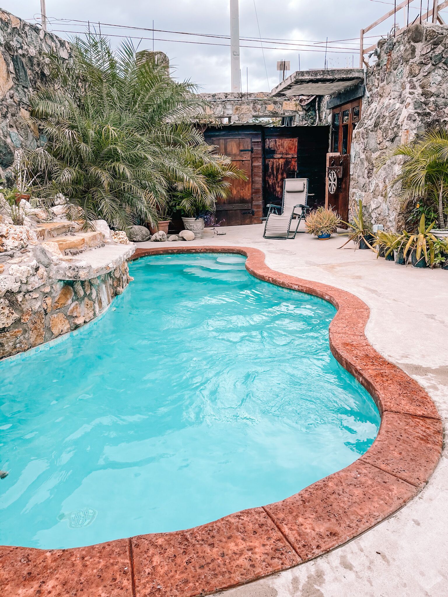 A swimming pool with a curved edge, surrounded by stone walls and potted plants.