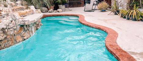 A swimming pool with a curved edge, surrounded by stone walls and potted plants.