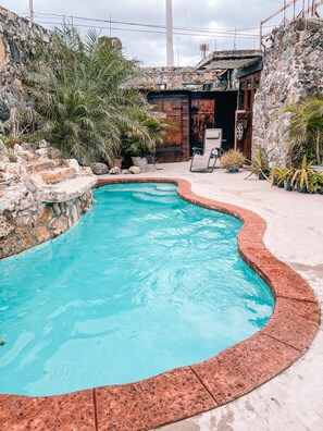 Une piscine à bord incurvé, entourée de murs en pierre et agrémentée de plantes en pot.