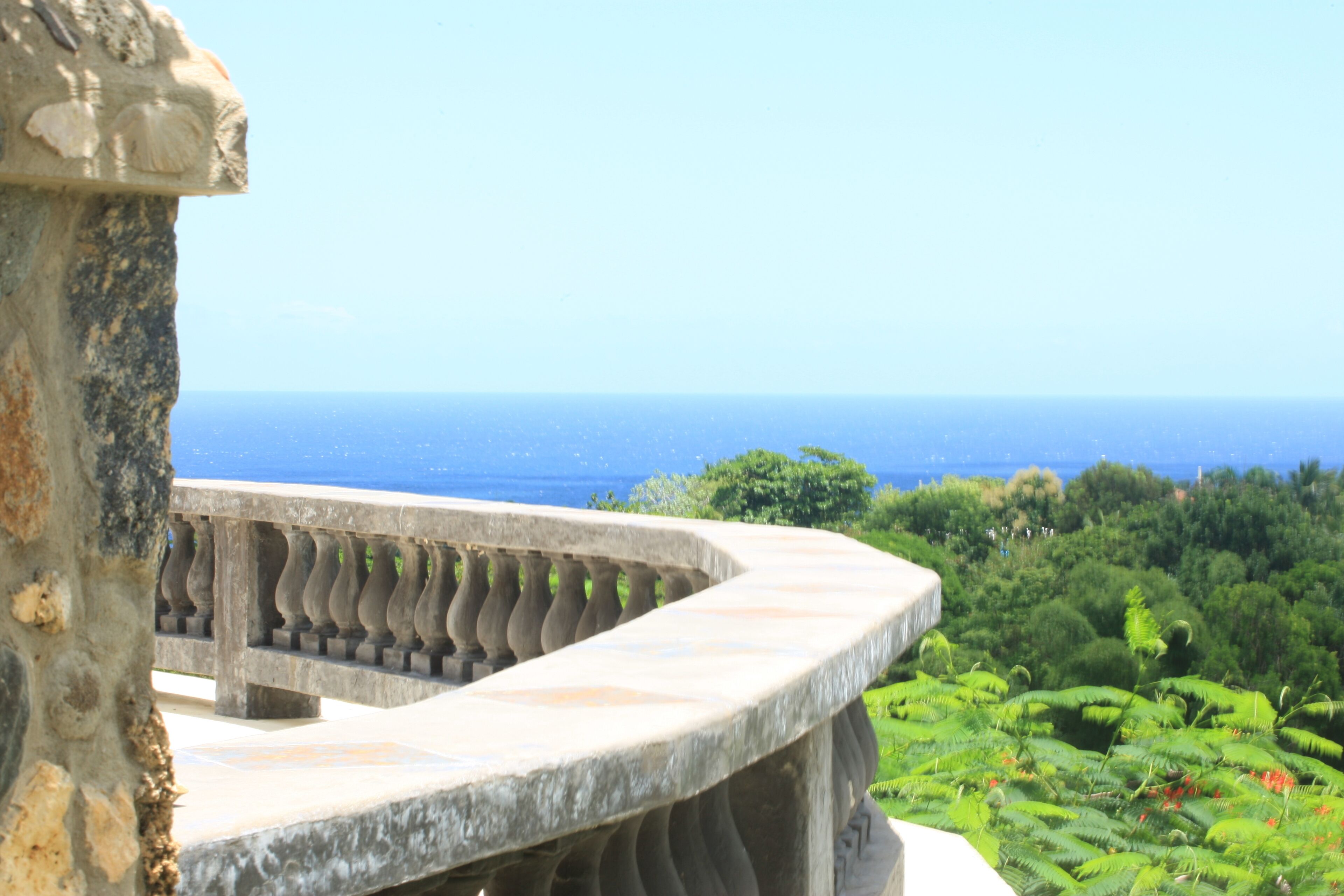 A stone balustrade overlooking a lush green landscape and the ocean.