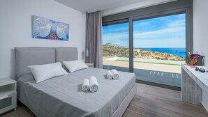 A modern bedroom with a large bed, a painting, a desk with sunglasses, and a view of the sea. - Villa Gaia (Rhodes)