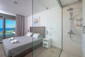 Ett modernt hotellrum med en stor säng, ett nattduksbord, en dusch och utsikt över havet.
