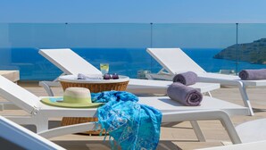 A sunlit outdoor lounge area with white lounge chairs, a wicker table with a drink, and a view of the sea. - Villa Gaia (Rhodes)