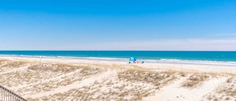 A beach with a sandy path leading to the water, a wooden fence, and a clear blue sky.