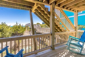 Eine Holzterrasse mit einer Treppe, die zu einer höheren Ebene führt, mit Blick auf einen Strand mit spärlicher Vegetation.