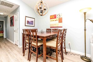 A dining area with a wooden table and chairs, a chandelier, a framed picture, and a poster on the wall. - Feels Like Home-3 BR Oceanfront Duplex; Covered Porches (Topsail Beach)