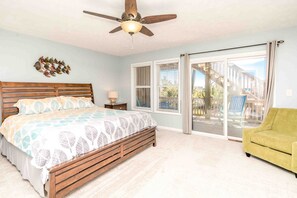 A bedroom with a bed, a ceiling fan, a nightstand, and a view through a sliding glass door to an outdoor deck. - Feels Like Home-3 BR Oceanfront Duplex; Covered Porches (Topsail Beach)