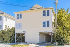 A two-story building with a garage entrance, a covered porch, and a sign that reads 'FEELS LIKE HOME.' - Feels Like Home-3 BR Oceanfront Duplex; Covered Porches (Topsail Beach)