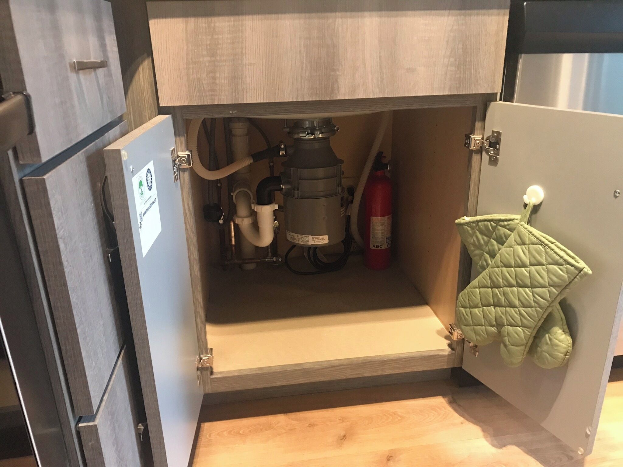 An open kitchen cabinet with visible plumbing and a fire extinguisher.