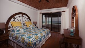 Un dormitorio con cama, ventilador de techo, vista al océano y una mesa de madera.