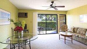 A room with a glass table, a sofa, a ceiling fan, and a sliding glass door leading to an outdoor area.