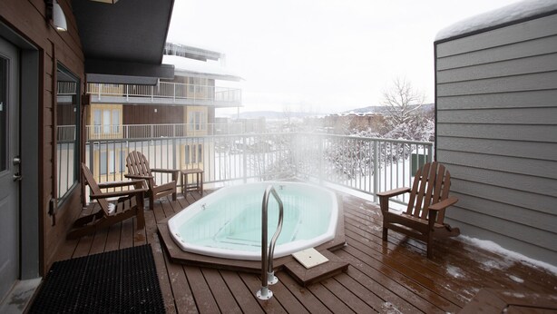 En træterrasse med et boblebad, to Adirondack-stole og udsigt til et snækkedække landskab.
