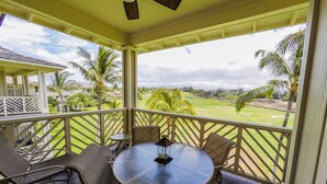 A covered outdoor area with a round table and chairs, overlooking a golf course with palm trees. - Quiet Top-floor Penthouse with Golf Course views, 2BR/2BA+Loft, Sleeps 6 (Puako)