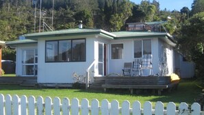 Una casa de un piso con techo verde, ventanas amplias y una terraza con mobiliario exterior.