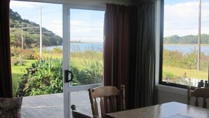 Una habitación con una mesa y sillas, vistas a un lago y vegetación, y una puerta con picaporte.