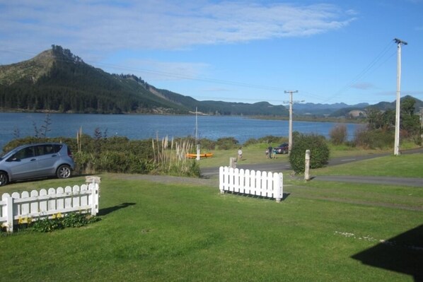 A grassy area with a white picket fence, a car, and a body of water in the background. - Opoutere - Nat's Place (Opoutere)