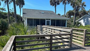 A wooden boardwalk leading to a house with a covered porch, surrounded by palm trees and greenery. - Oceanfront Home on Folly Beach, SC (Folly Beach)