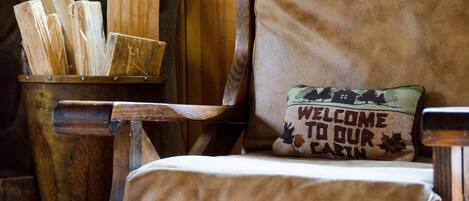 A rustic cabin interior with a wooden chair and a welcome sign pillow.