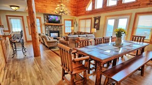 Un salón espacioso con chimenea, un comedor con una gran mesa de madera y bancos, y una zona de estar acogedora con sillas estampadas.