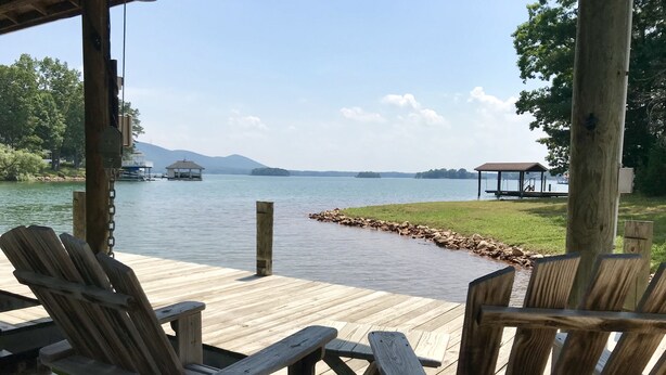 Una terraza de madera con sillas Adirondack con vistas a un lago, un muelle y un pabellón.