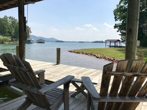 Una terraza de madera con sillas Adirondack con vistas a un lago, un muelle y un pabellón.