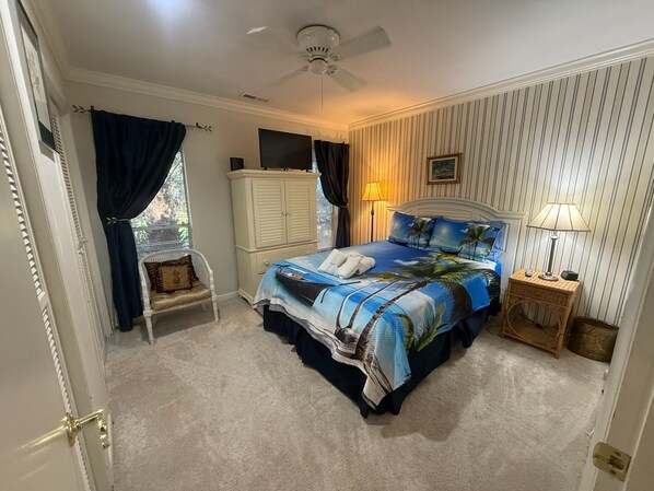 A bedroom with a bed, a ceiling fan, a nightstand, a lamp, a wardrobe, and a window with curtains.