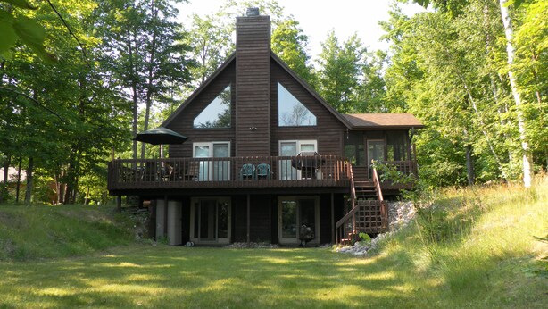 A cabin with a large deck, a chimney, and a staircase leading to an upper level.