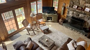 A cozy cabin interior with a stone fireplace, wooden furniture, and a television. - Bear Beach Maine! Oceanfront Log Cabin, Secluded Sandy Beach, Sunsets & Sauna (Cutler)