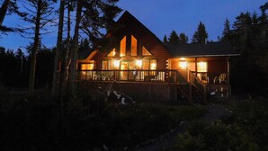 A log cabin with a large deck and multiple windows, surrounded by trees. - Bear Beach Maine! Oceanfront Log Cabin, Secluded Sandy Beach, Sunsets & Sauna (Cutler)