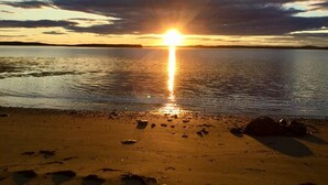A beach at sunset with the sun reflecting on the water. - Bear Beach Maine! Oceanfront Log Cabin, Secluded Sandy Beach, Sunsets & Sauna (Cutler)