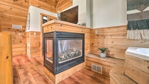 L’intérieur d’un chalet en bois est doté d’une cheminée, de murs en bois et d’une petite salle de bain avec un lavabo et une plante en pot.
