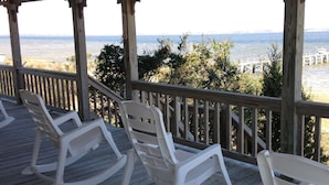 Une terrasse en bois avec des fauteuils à bascule blancs, donnant sur la plage.