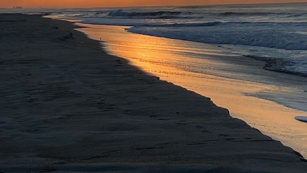 Une plage au coucher du soleil, avec des vagues qui se rapprochent du rivage.