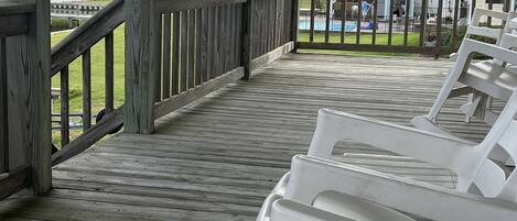 A wooden deck with white plastic chairs, overlooking a marina and a building with a balcony.