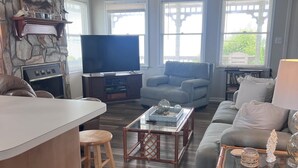 Un salon moderne doté d’une cheminée en pierre, d’un téléviseur à écran plat, d’un canapé gris, d’une table basse et d’un coin repas avec des tabourets.