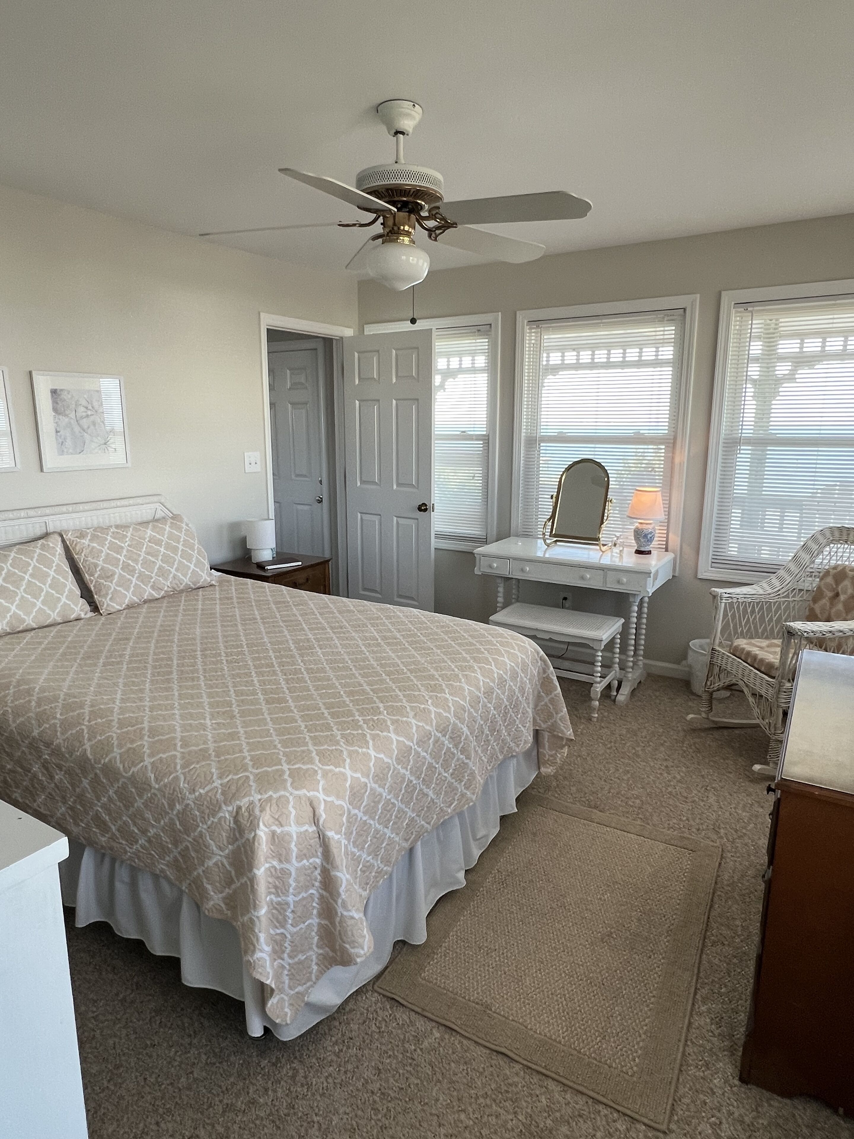 A bedroom with a bed, a vanity with a mirror, a chair, and a ceiling fan.